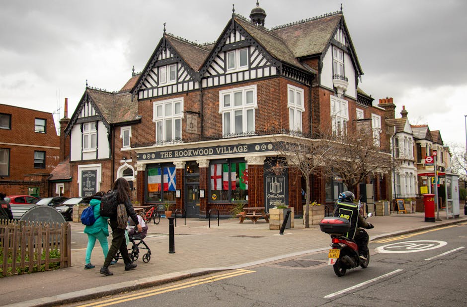 A traditional three-story brick pub with black-and-white timber framing signage reading 'The Rookwood Village' is situated on a street corner in South Norwood SE25. The pub features large windows, som