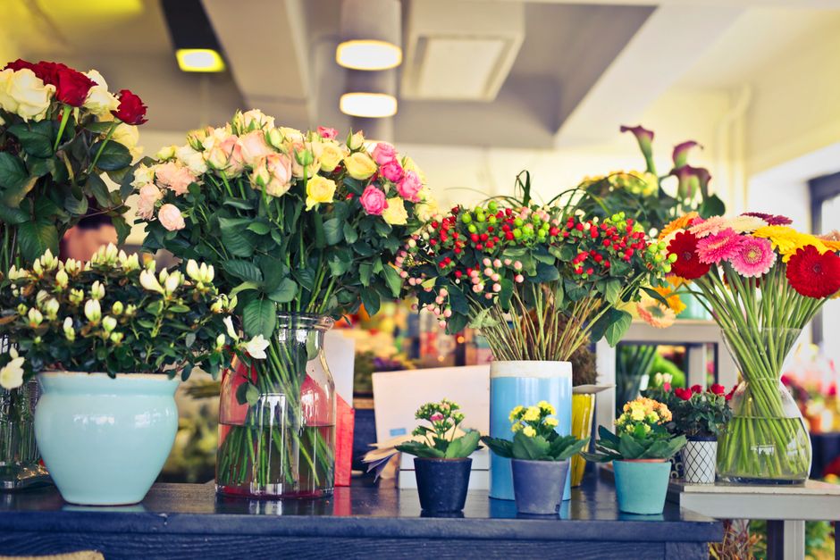 An arrangement of multiple flower bouquets displayed on a wooden table at a flower shop, featuring a variety of fresh flowers including pink and white roses, red and pink gerbera daisies, white and ye